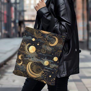 May include: A black tote bag with a gold and black celestial pattern. The pattern features moons, stars, and swirling clouds.