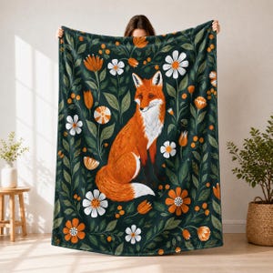 May include: A dark green blanket with a design of an orange fox, white and orange flowers, and green leaves. The fox is depicted sitting. The blanket has a floral pattern.
