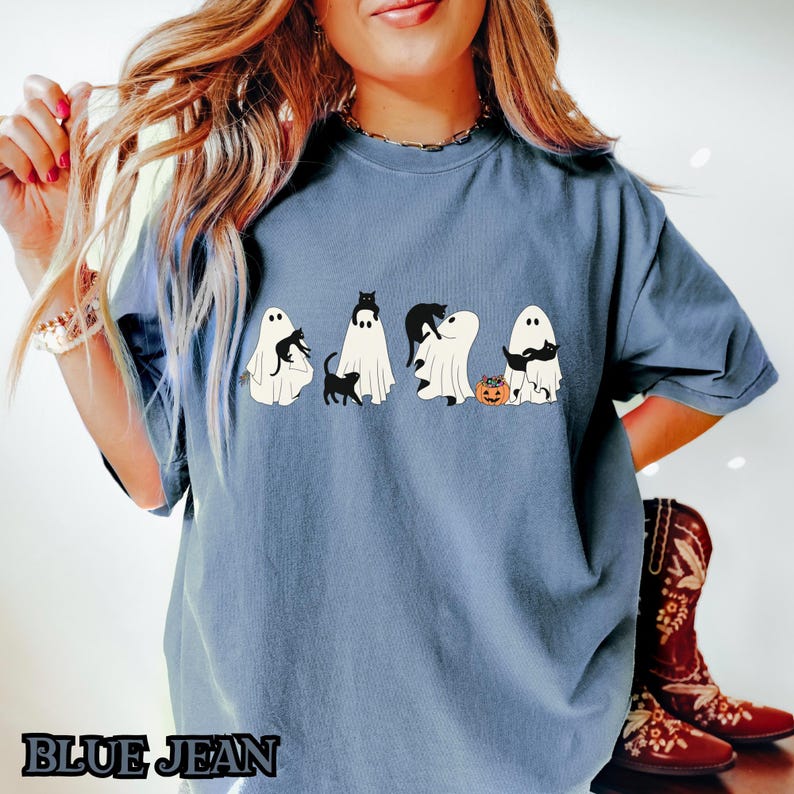 K&ouml;nnte beinhalten: Ein blaues T-Shirt mit einem Aufdruck von f&uuml;nf Geistern, die schwarze Katzen halten. Die Geister tragen einen K&uuml;rbis und einige halten eine Katze in ihren Armen.