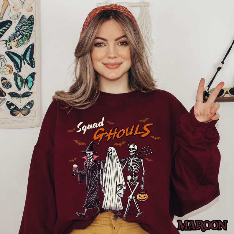 Pu&ograve; includere: Una felpa color granata con una grafica di tre scheletri vestiti da ghoul. Il testo "Squad Ghouls" &egrave; stampato sopra gli scheletri.