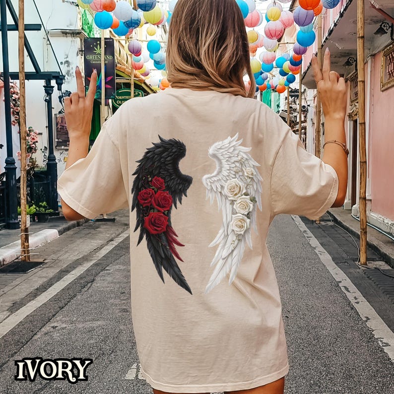 May include: A beige t-shirt with a graphic of black and white angel wings with red and white roses on each wing. The text "IVORY" is at the bottom of the image.