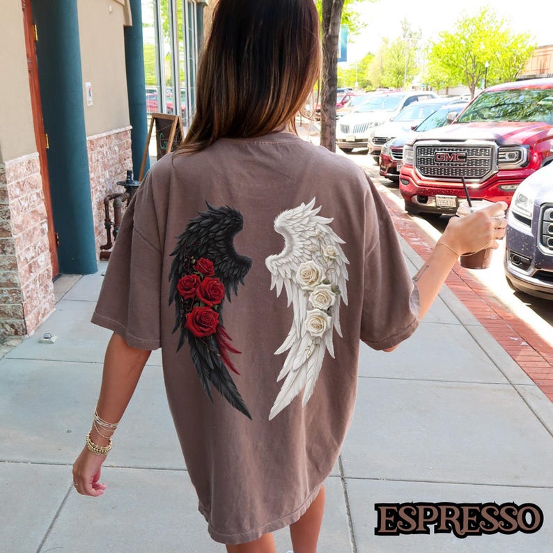May include: A brown oversized t-shirt with a graphic of black and white angel wings with red roses on the black wing. The wings are centered on the back of the shirt.