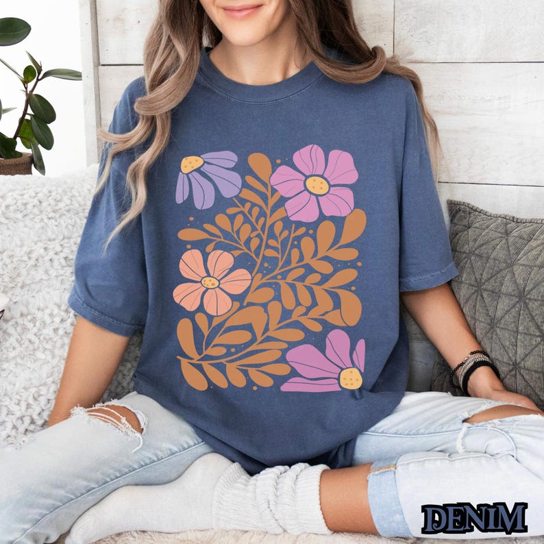 Op de afbeelding: Een marineblauw t-shirt met een bloemenprint met roze, oranje en paarse bloemen met bruine stelen en bladeren.