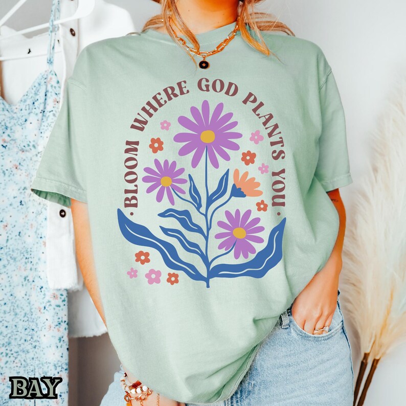 May include: A light green t-shirt with a floral design and the text "Bloom where God plants you."