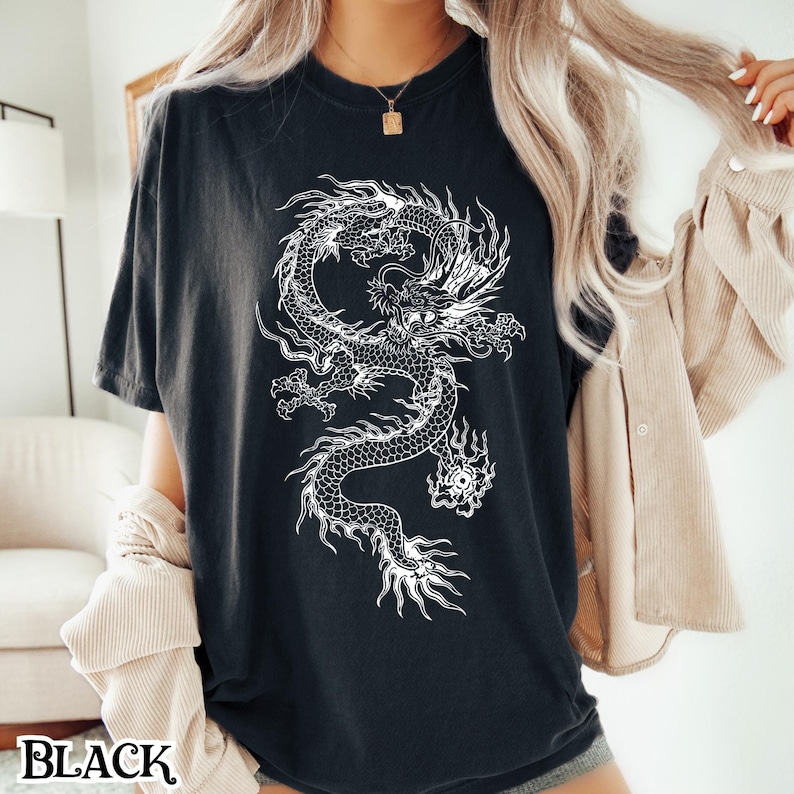 May include: A black t-shirt with a white graphic of a dragon. The dragon is curled up with its head facing the viewer. The t-shirt is a relaxed fit and has a crew neck.