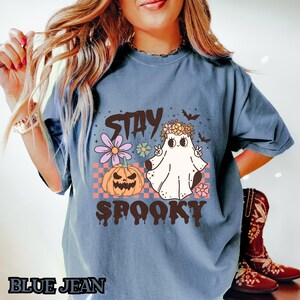 K&ouml;nnte beinhalten: Ein blaues T-Shirt mit einem Aufdruck eines Geistes, der eine Blumenkrone tr&auml;gt und ein Peace-Zeichen macht. Der Text "Stay Spooky" ist unter dem Geist gedruckt.