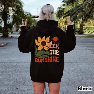 K&ouml;nnte beinhalten: Schwarzer Kapuzenpullover mit einem Sonnenblumen-Motiv und dem Text "Seek the Sunshine" auf der R&uuml;ckseite.
