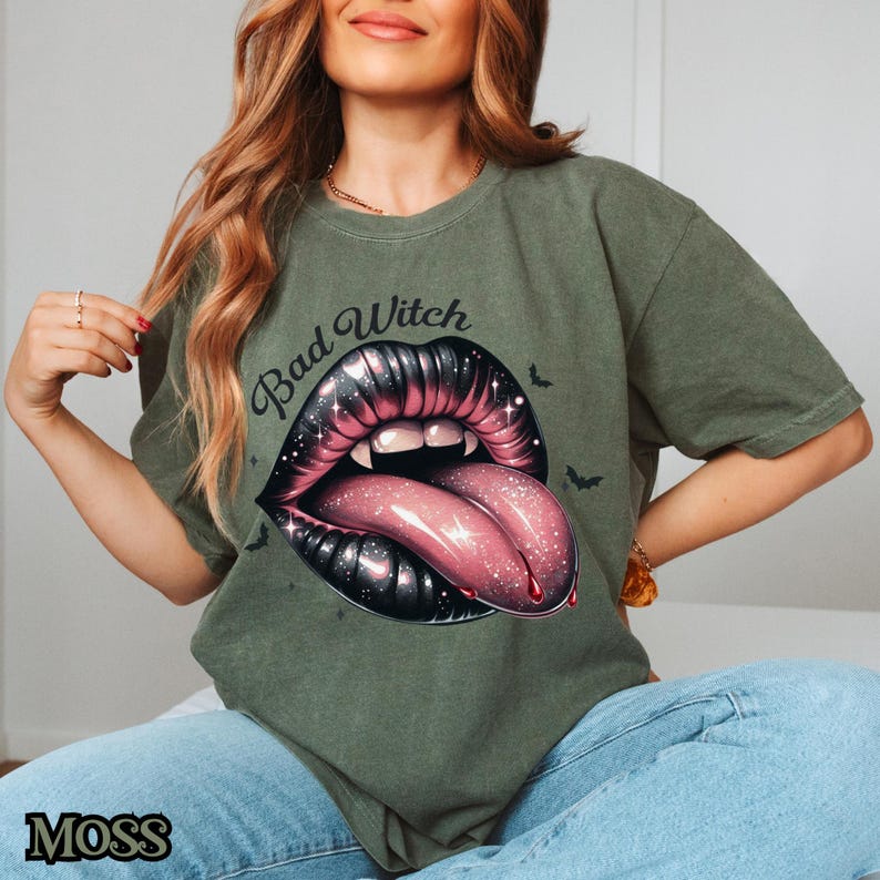 Peut inclure: Un t-shirt vert avec le texte "Bad Witch" et un graphique d'une bouche noire et rose avec une langue qui sort.