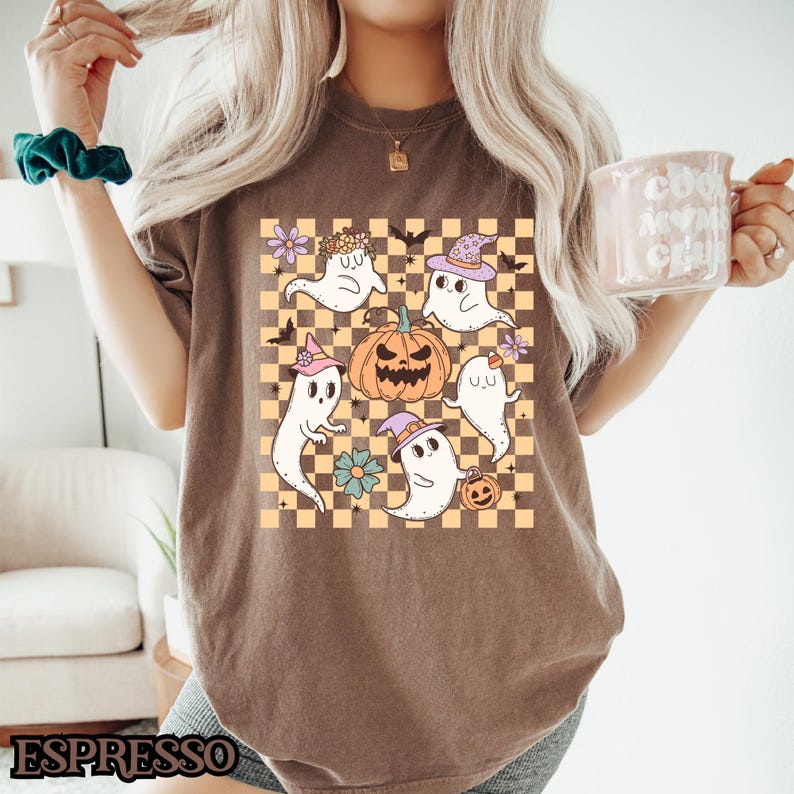 May include: A brown t-shirt with a checkered pattern featuring a group of cartoon ghosts and a jack-o-lantern. The ghosts are wearing hats and holding pumpkins.