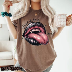 Peut inclure: Un t-shirt marron avec un graphique d'une bouche noire et rouge avec une langue qui sort. Le texte "Bad Witch" est imprim&eacute; au-dessus de la bouche.