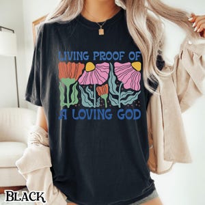 May include: Black t-shirt with a graphic of colorful flowers and the text "Living Proof of a Loving God".