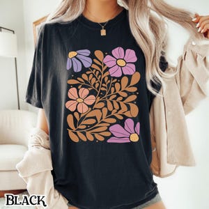 Op de afbeelding: Zwart T-shirt met een bloemenprint met roze, paarse en oranje bloemen met bruine stelen en bladeren.