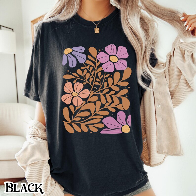 Op de afbeelding: Zwart T-shirt met een bloemenprint met roze, paarse en oranje bloemen met bruine stelen en bladeren.