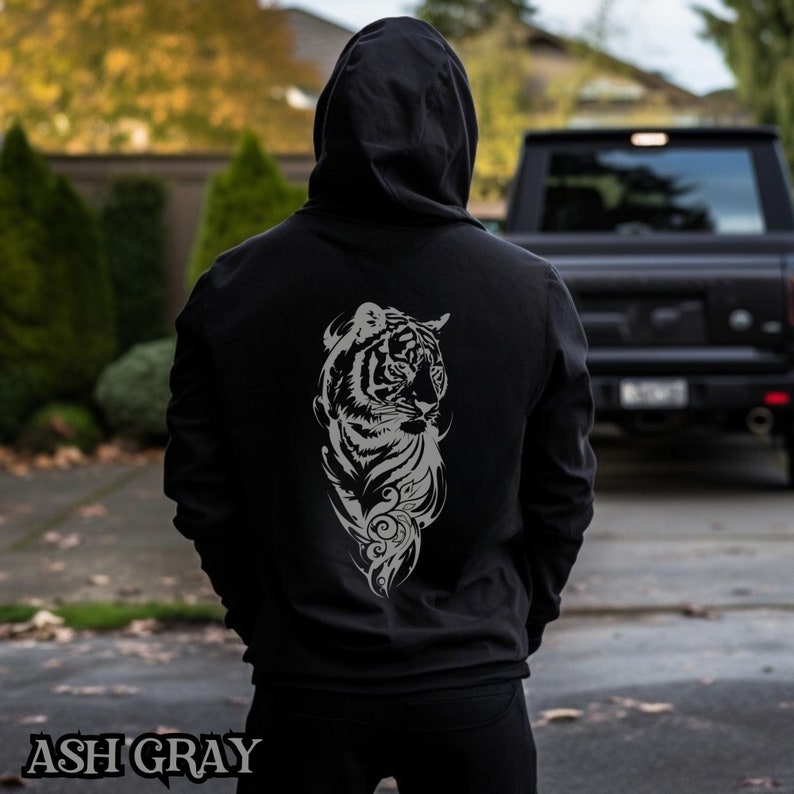 May include: A black hoodie with a gray tiger graphic on the back. The tiger is facing to the left and has a floral design around it. The hoodie is ash gray.