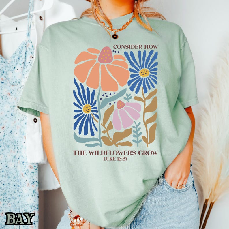 May include: A light green t-shirt with a floral design and the text "Consider how the wildflowers grow Luke 12:27".