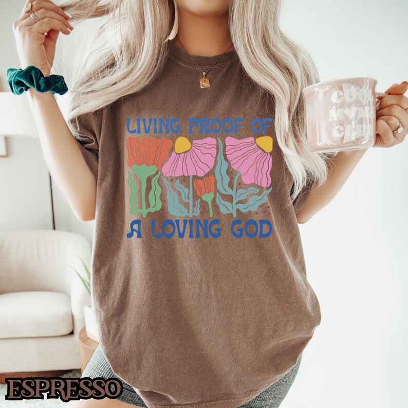 May include: A brown t-shirt with a graphic of colorful flowers and the text "Living Proof of a Loving God".