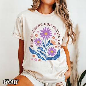 May include: A cream-coloured t-shirt with a floral design and the text "Bloom where God plants you."