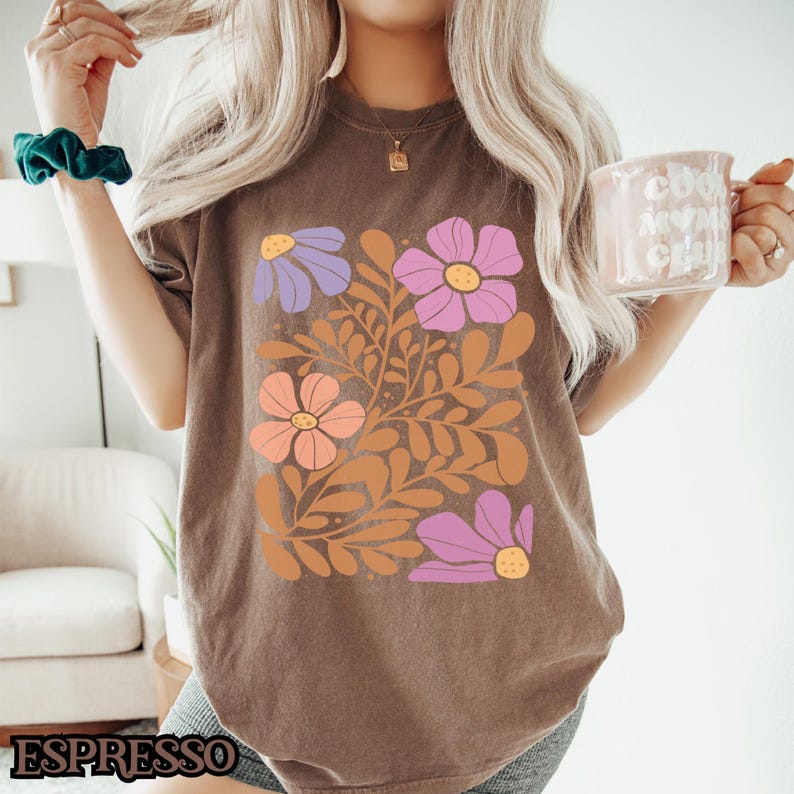Op de afbeelding: Een bruin T-shirt met een bloemenprint met roze, paarse en oranje bloemen met bruine stelen en bladeren.