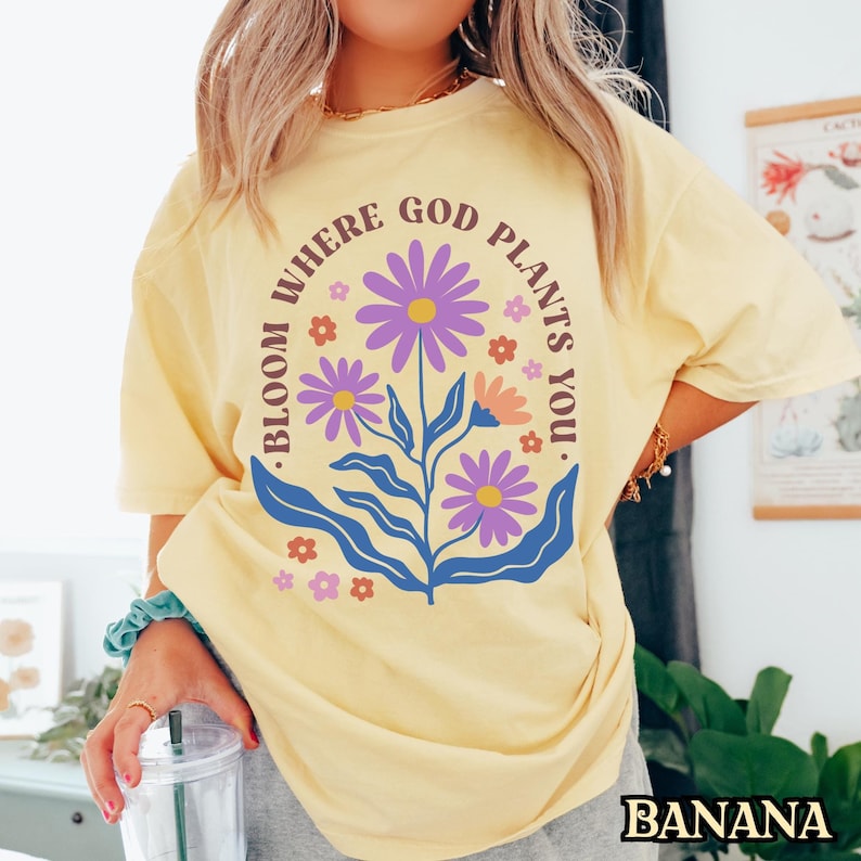 May include: A yellow t-shirt with a floral design and the text "Bloom Where God Plants You."