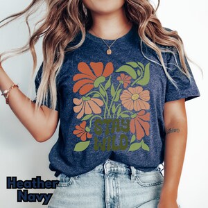 May include: A heather navy blue t-shirt with a floral design and the text "Stay Wild" in green.