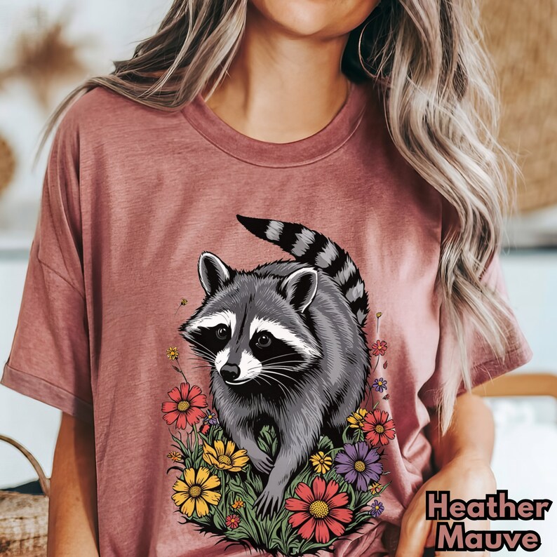 May include: A heather mauve t-shirt with a graphic of a raccoon surrounded by colorful flowers.
