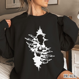 May include: Black sweatshirt with a white graphic of a skull with hands reaching out from behind it.