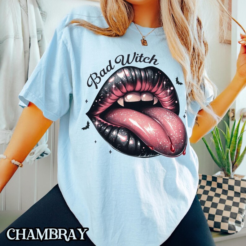 Peut inclure: T-shirt bleu clair avec un graphique d'une bouche noire et rose avec une langue qui sort et le texte "Bad Witch" au-dessus.
