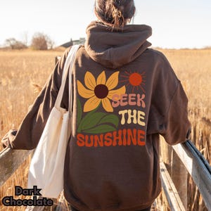 K&ouml;nnte beinhalten: Ein brauner Hoodie mit einem Sonnenblumen-Motiv und dem Text "Seek the Sunshine" auf der R&uuml;ckseite.