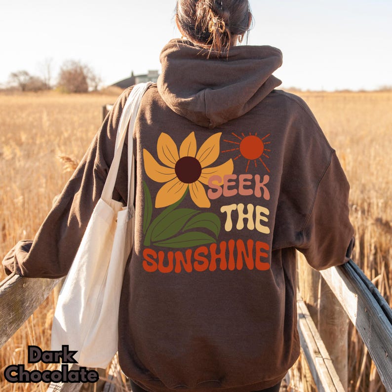 K&ouml;nnte beinhalten: Ein brauner Hoodie mit einem Sonnenblumen-Motiv und dem Text "Seek the Sunshine" auf der R&uuml;ckseite.