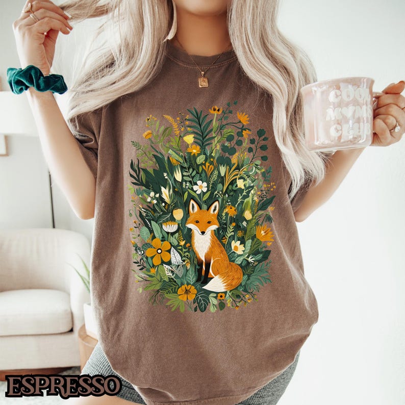 May include: A brown t-shirt with a graphic of a fox sitting in a field of flowers. The fox is orange and white, and the flowers are yellow, pink, and green.