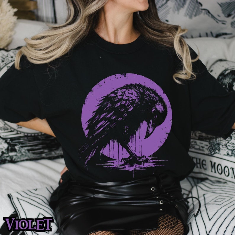 May include: A black t-shirt with a purple circle graphic of a black raven. The raven is perched on a branch with its wings spread out.