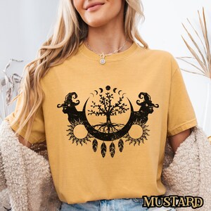 May include: A yellow t-shirt with a black graphic of a tree with roots, moons, and suns. The graphic has a vintage, distressed look.
