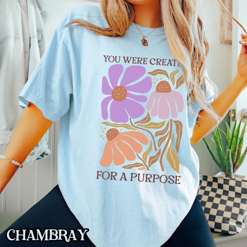 May include: A light blue t-shirt with a floral design and the text "You were created for a purpose".