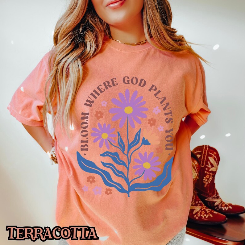 May include: A peach-coloured t-shirt with a floral design and the text "Bloom Where God Plants You."