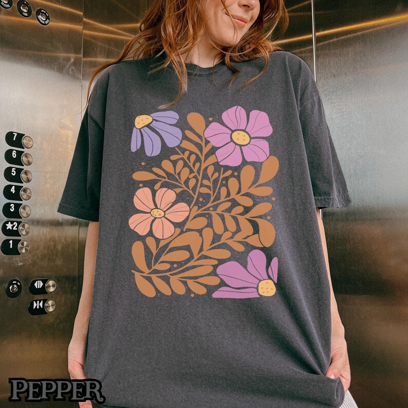 Op de afbeelding: Een zwart T-shirt met een bloemenprint met roze, paarse en bruine bloemen op een donkere achtergrond.