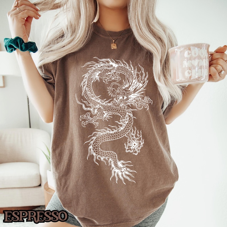 May include: A brown t-shirt with a white graphic of a dragon. The dragon is curled up with its head facing the right side of the image.