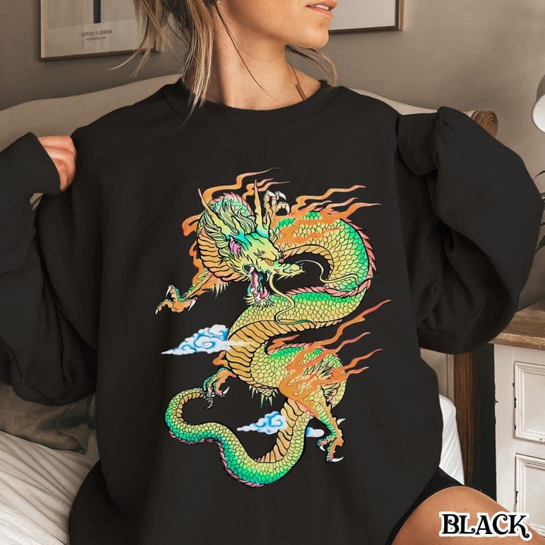 K&ouml;nnte beinhalten: Schwarzes Sweatshirt mit einem bunten Grafikdruck eines Drachen mit Flammen. Der Drache ist gr&uuml;n, gelb und orange.