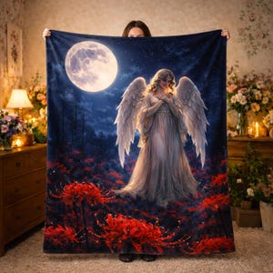 May include: A plush blanket featuring a celestial scene with an angel, a full moon, and red flowers. The angel has large white wings and is wearing a flowing gown. The background is a dark blue night sky with a forest.