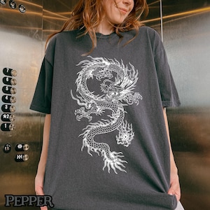 May include: A dark gray t-shirt with a white graphic of a dragon. The dragon is detailed with scales and has a fierce expression.