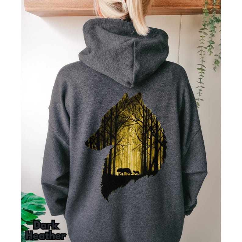 May include: A dark heather gray hooded sweatshirt featuring a large graphic on the back. The graphic is a silhouette of a wolf head filled with a yellow and black forest scene, depicting a wolf and a smaller pup walking among tall trees.
