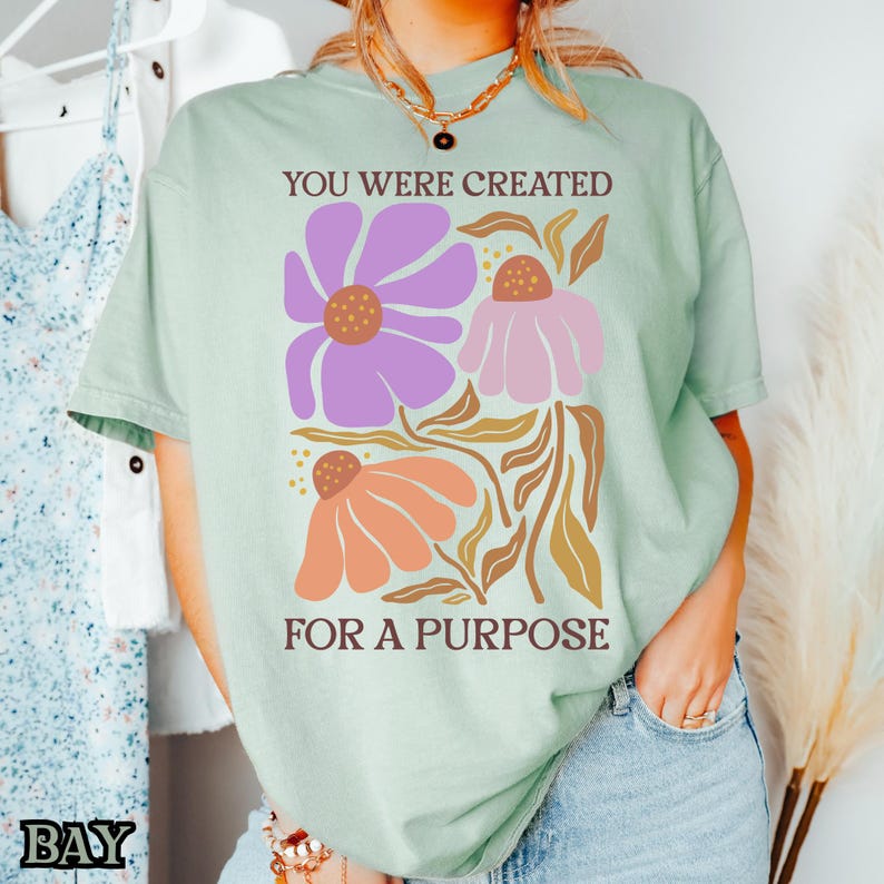 May include: A light green t-shirt with a floral design and the text "You were created for a purpose".