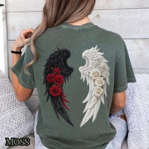 May include: A green t-shirt with a black and white angel wing design. The wings are adorned with red and white roses.