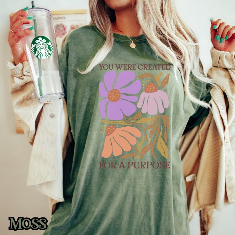 May include: A green t-shirt with a floral design and the text "You were created for a purpose".