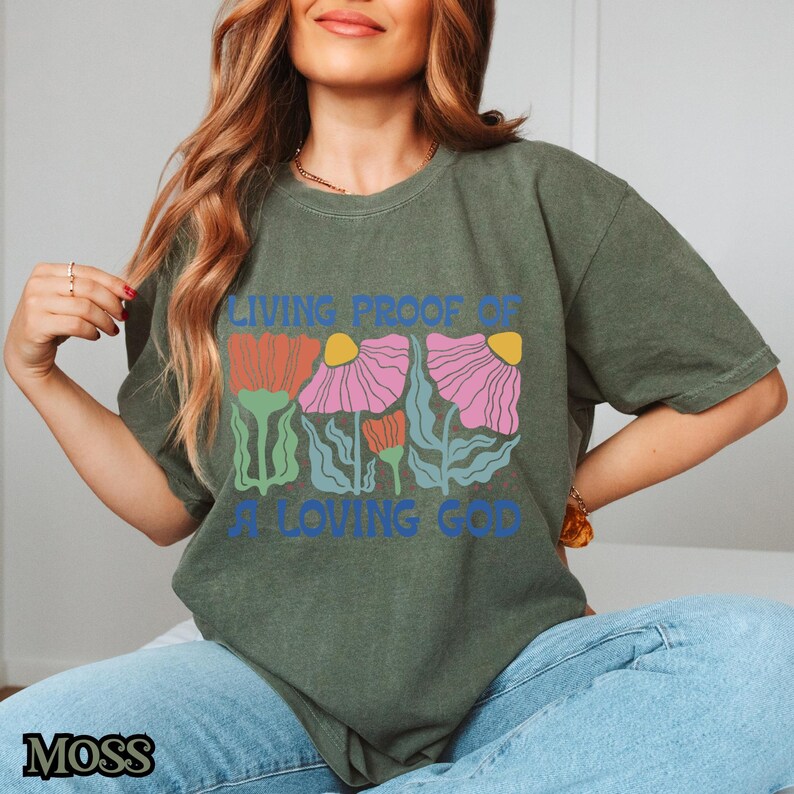 May include: A green t-shirt with a floral design and the text "Living Proof of a Loving God".