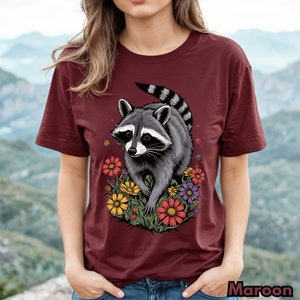 May include: A maroon t-shirt with a graphic of a raccoon walking through a field of colorful flowers.