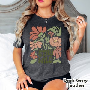 May include: Dark grey heather t-shirt with a floral design and the text "Stay Wild" in a retro font.