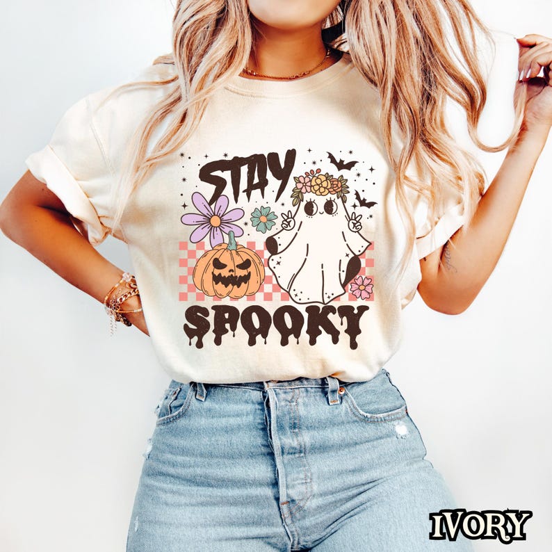 K&ouml;nnte beinhalten: Ein wei&szlig;es T-Shirt mit einem Aufdruck eines Geisters, der eine Blumenkrone tr&auml;gt und ein Peace-Zeichen macht. Der Geist befindet sich neben einem K&uuml;rbis und der Text "Stay Spooky" befindet sich unter dem Aufdruck.