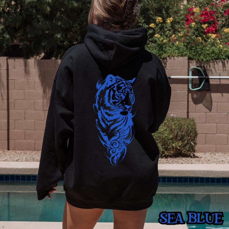 May include: A black hoodie with a blue tiger graphic on the back. The tiger is facing to the right and has a detailed design with feathers and swirls.