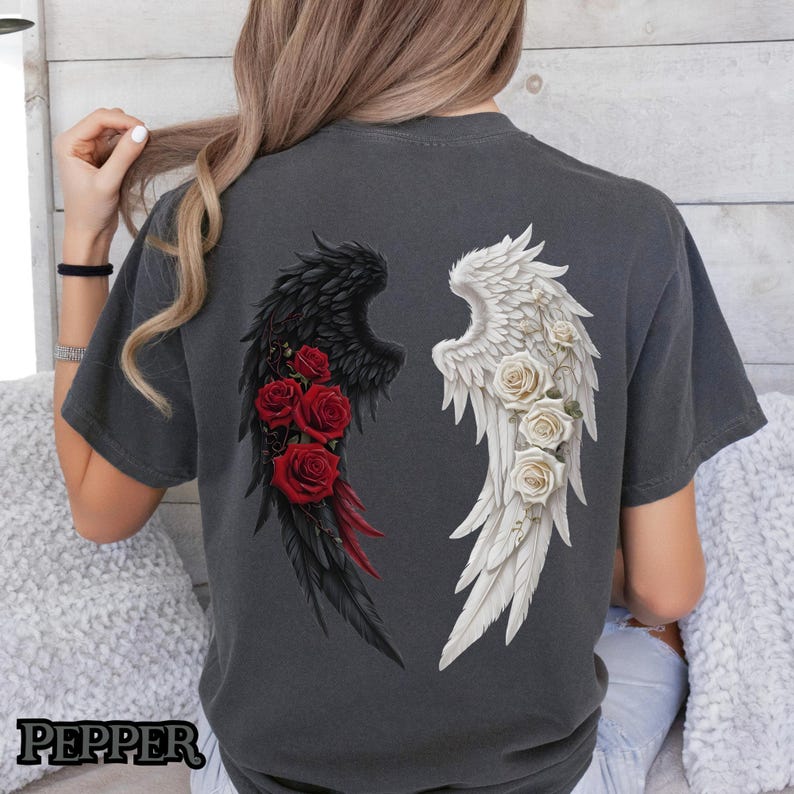 May include: A dark gray t-shirt with a black and white angel wing design. The wings are adorned with red roses.