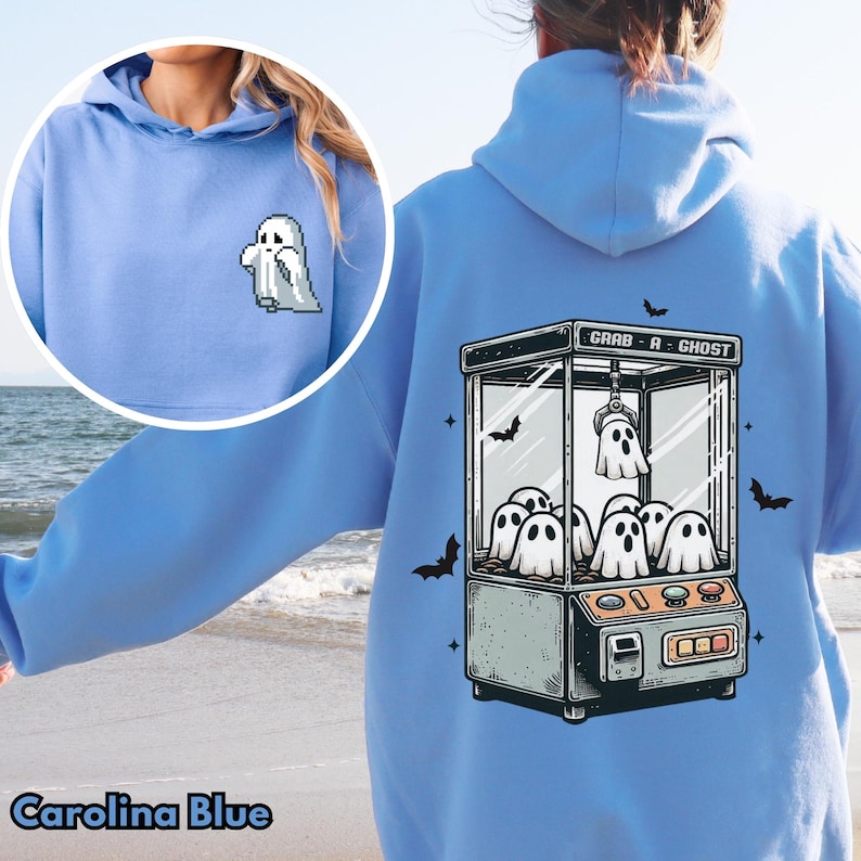 Pode incluir: Um moletom azul claro com um gr&aacute;fico de uma m&aacute;quina de garras fantasma com o texto "Grab-A-Ghost". O moletom tem um pequeno gr&aacute;fico de fantasma na frente.